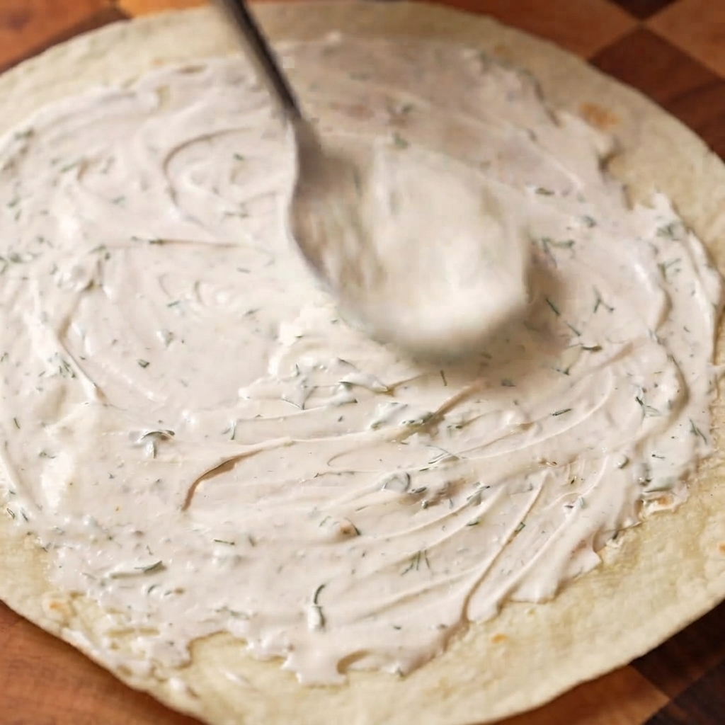 Sauce à la crème sûre à laneth étalée uniformément sur un wrap de blé avec une cuillère.