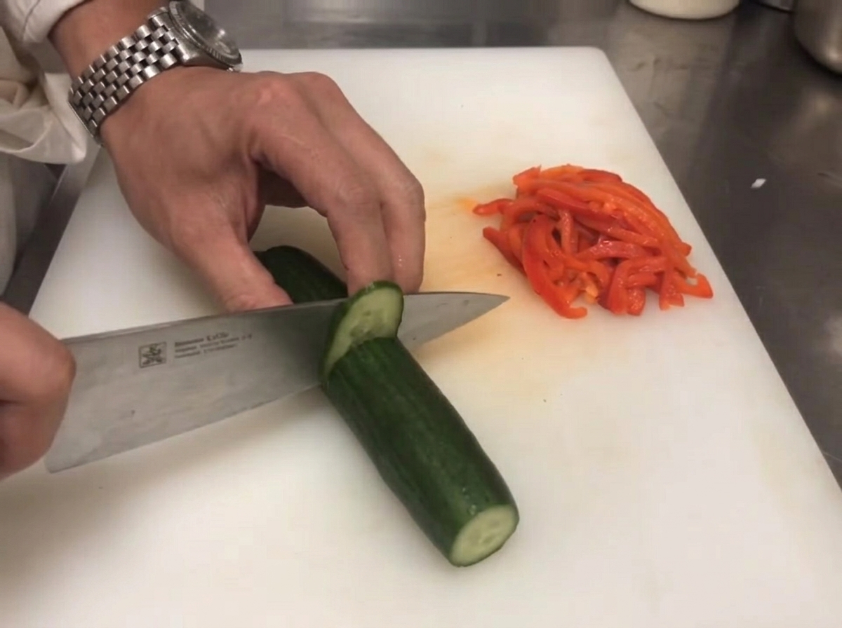 Un couteau coupant un concombre vert frais à côté de poivrons rouges tranchés.