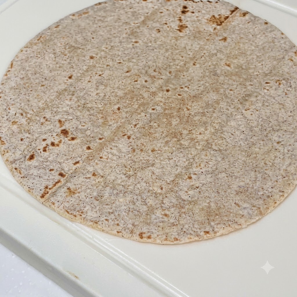 Une tortilla de blé entier garnie de sauce au beurre de cacahuète, de poulet tranché, de chou rouge et de laitue fraîche.