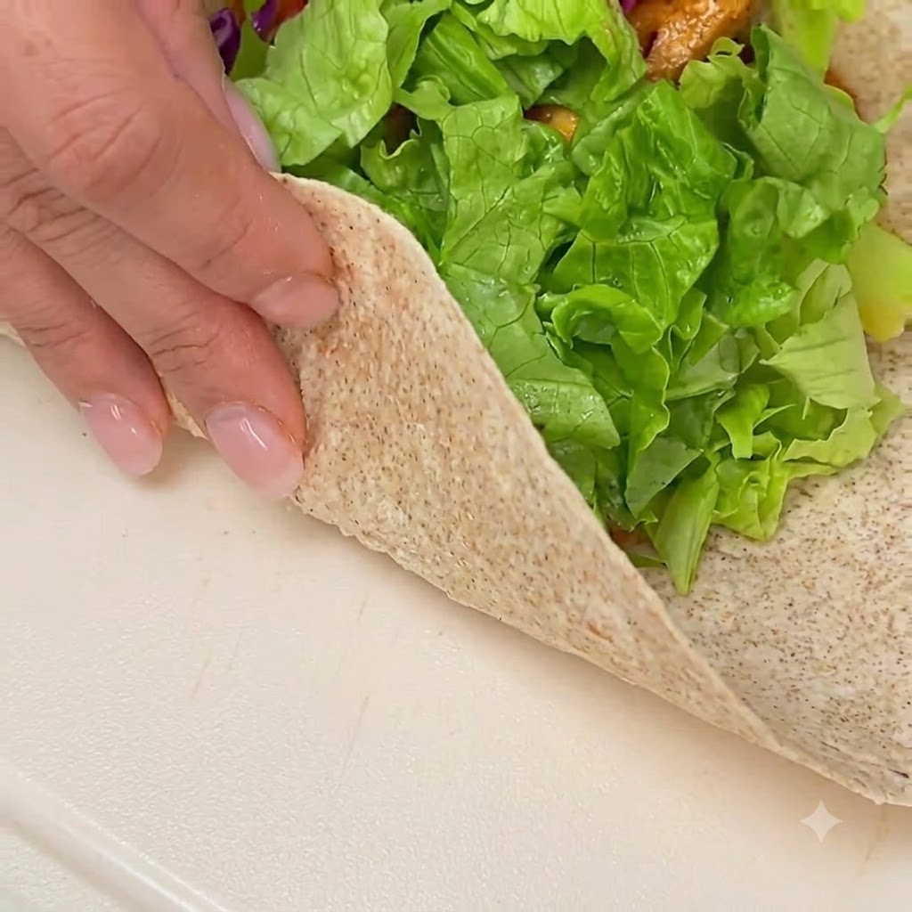 Mains pliant et roulant une tortilla de blé entier garnie sur une surface blanche propre.