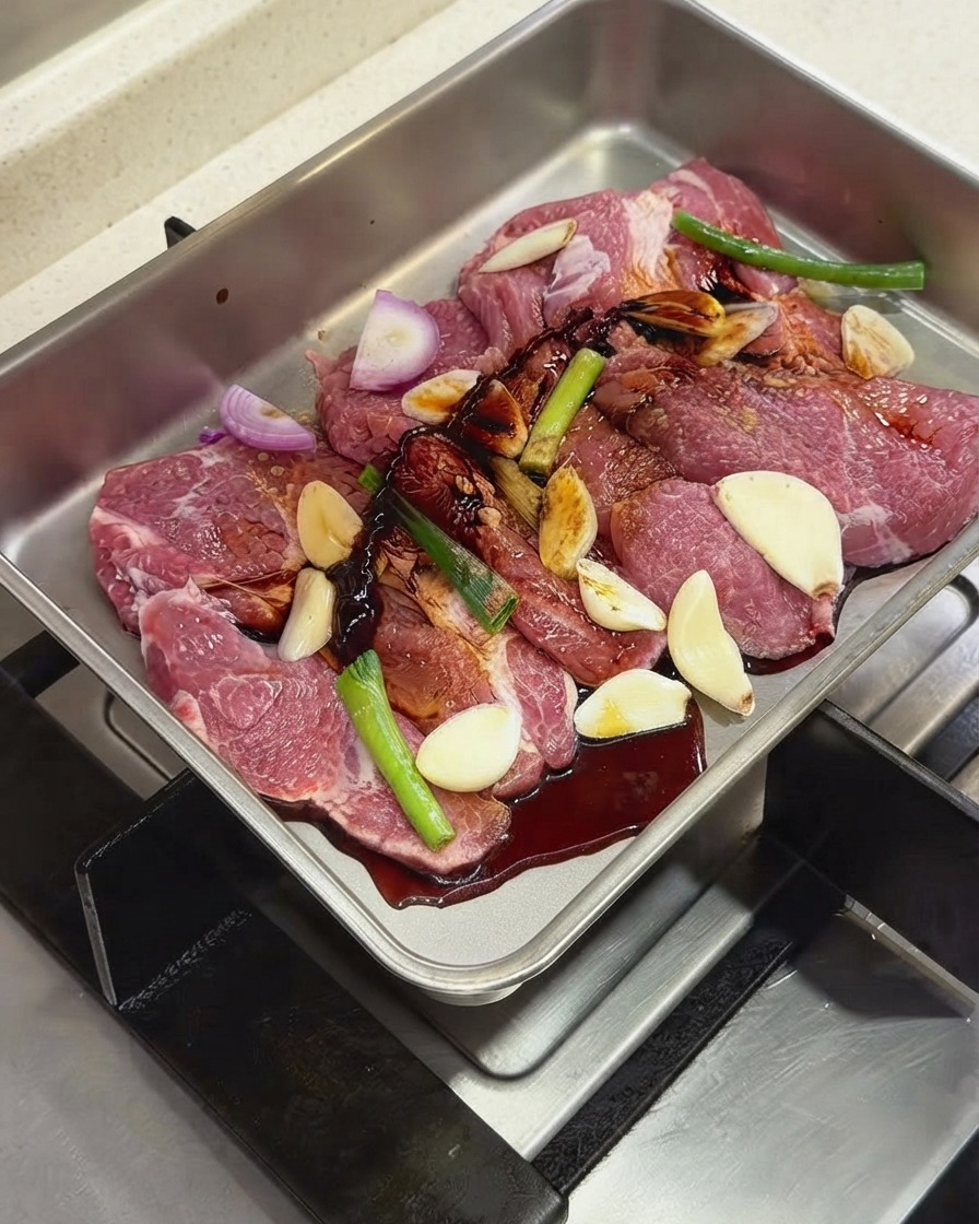 Sauces foncées et assaisonnements versés sur les côtes de porc et les aromates dans un plat en métal.