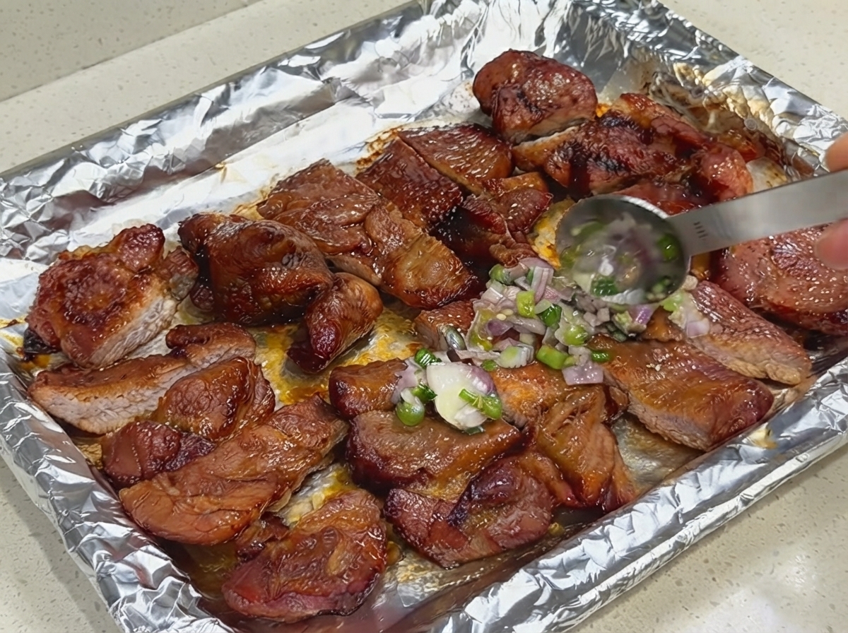 Cuillère appliquant une couche de sauce fraîche aux oignons verts et aux échalotes sur le porc tranché posé sur une feuille de cuisson.