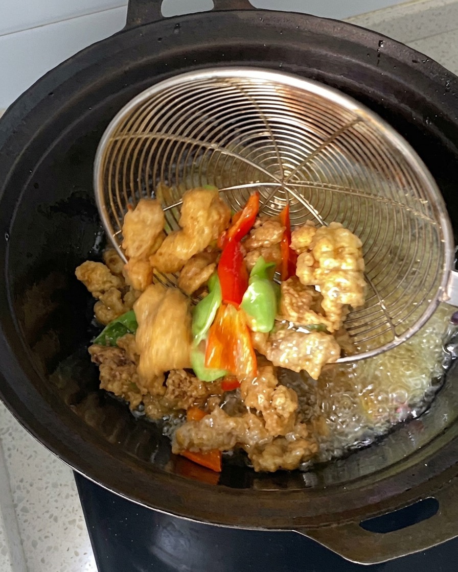 Des morceaux de viande marinés et des piments plongés et ramassés à laide dune écumoire en fil de fer dans un wok dhuile chaude.