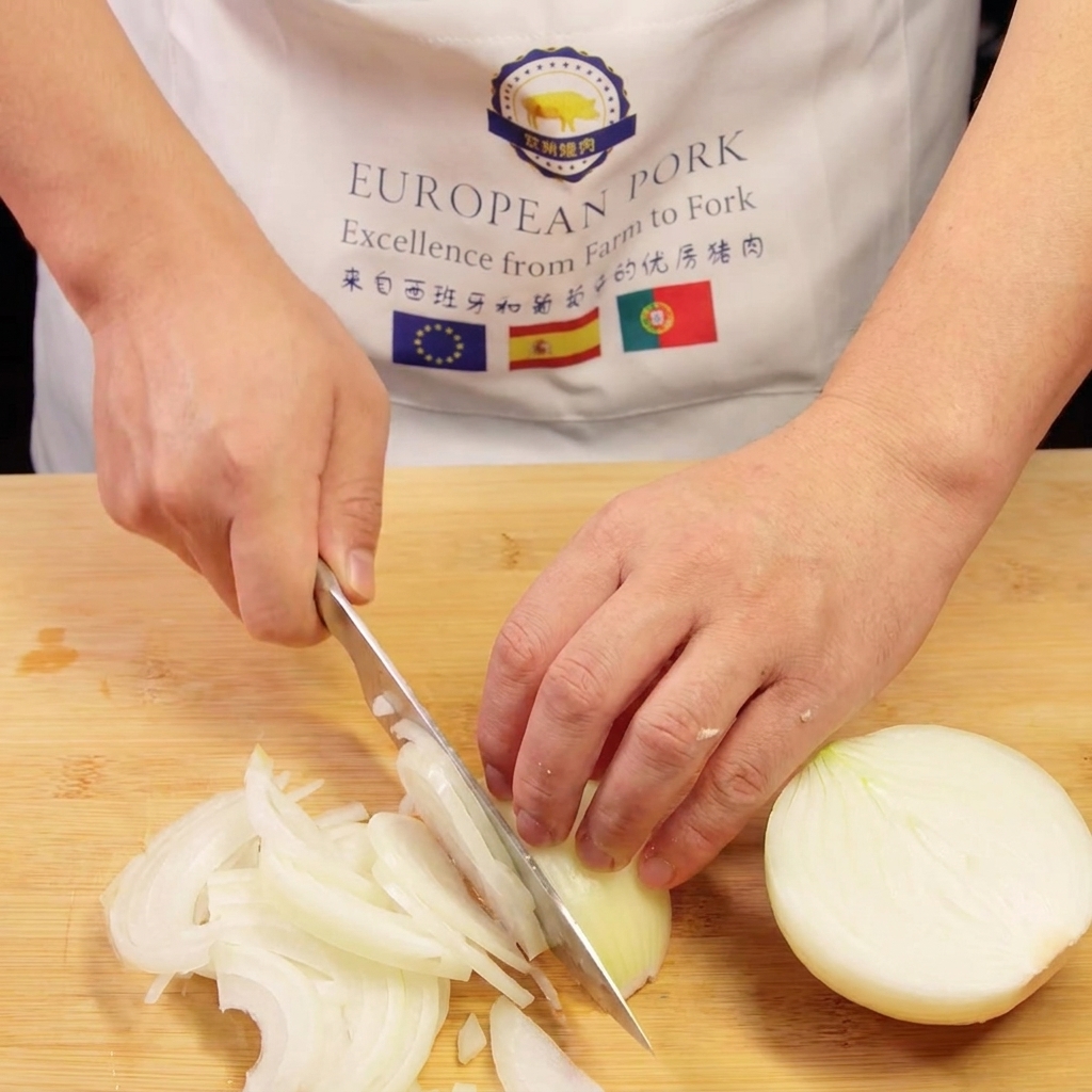 Les mains dun chef tranchant un oignon en fines lanières sur une planche à découper en bois.