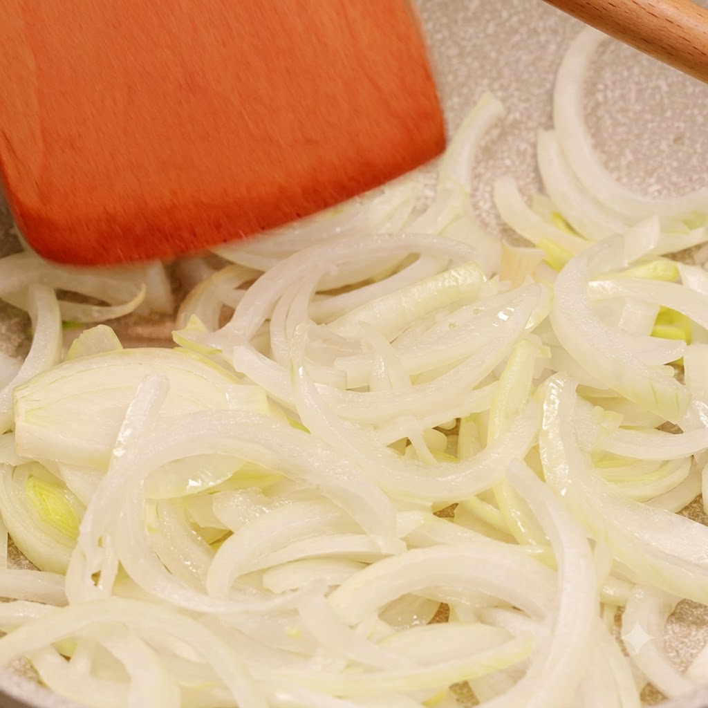 Oignons émincés cuisant dans une poêle et remués avec une spatule en bois.