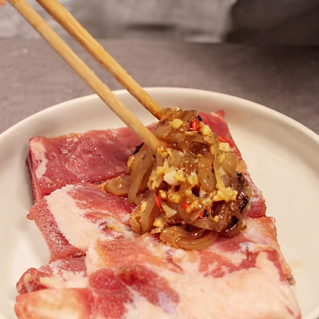 Des baguettes tenant une portion du mélange doignons et de sauce sur des travers de porc crus sur une assiette blanche.