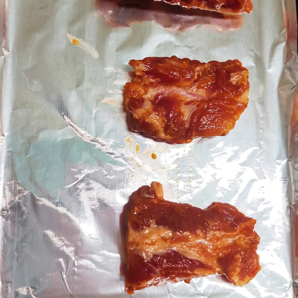 Morceaux de côtes de porc marinées disposés soigneusement sur une seule rangée sur une plaque de cuisson recouverte de papier daluminium.