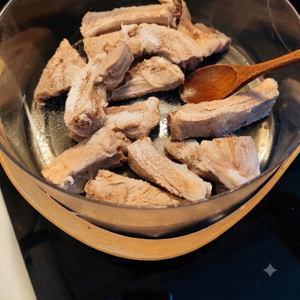 Une cuillère en bois posée sur des travers de porc blanchis saupoudrés de sel et dassaisonnements dans une casserole.