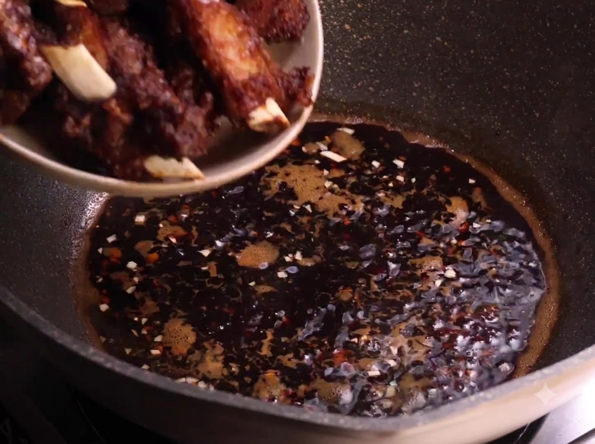 Travers de porc fris transférés dune assiette vers la sauce foncée frémissante dans un wok.