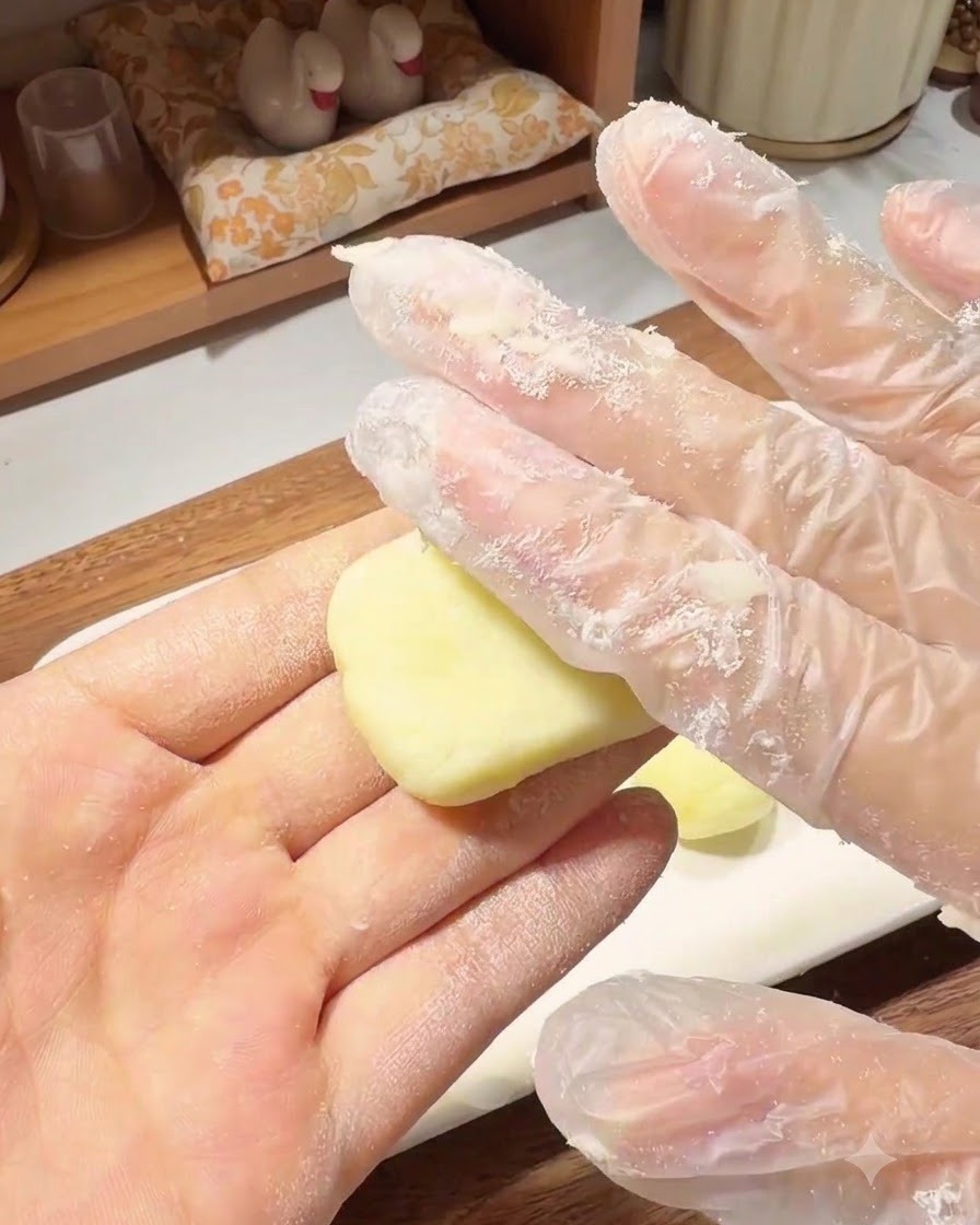 Une main gantée pressant une petite boule de pâte de pommes de terre pour lui donner une forme de galette ronde et plate dans le creux de la main.