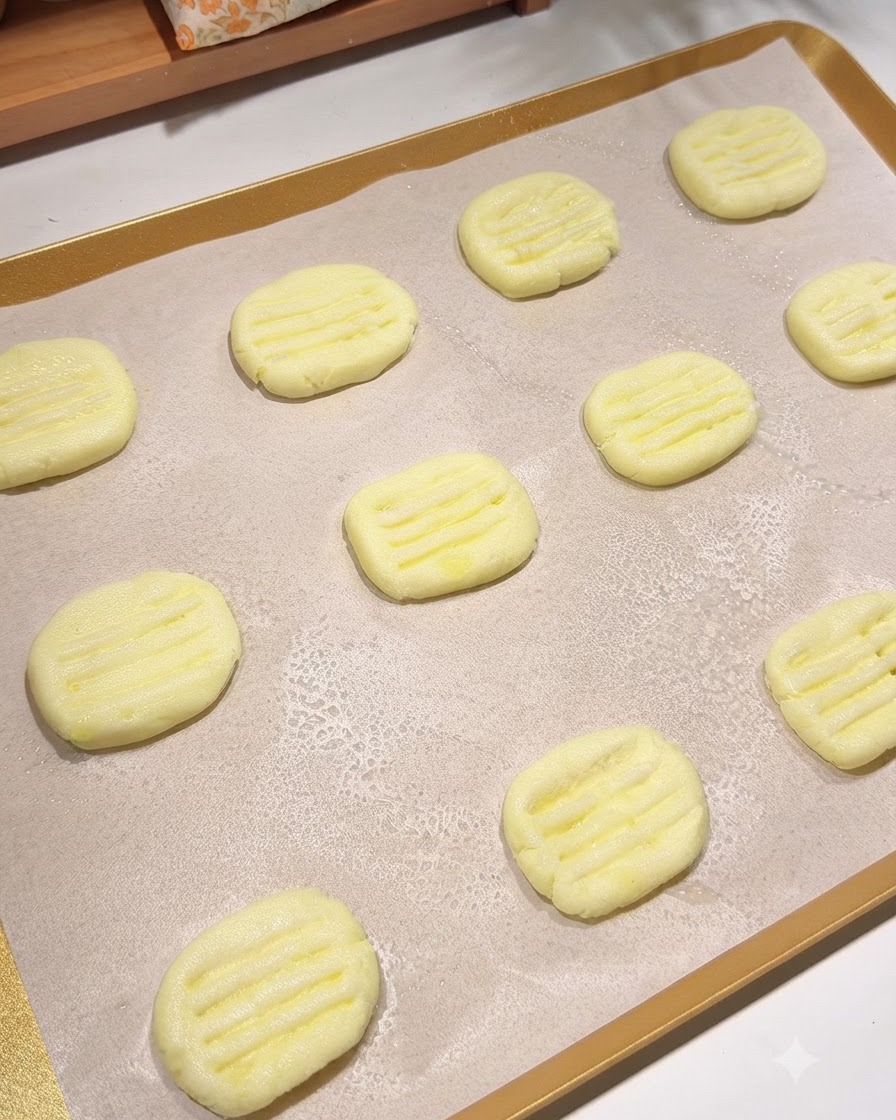 Une plaque de cuisson recouverte de papier sulfurisé contenant plusieurs galettes de pommes de terre façonnées avec une fine brume dhuile de cuisson vaporisée par-dessus.