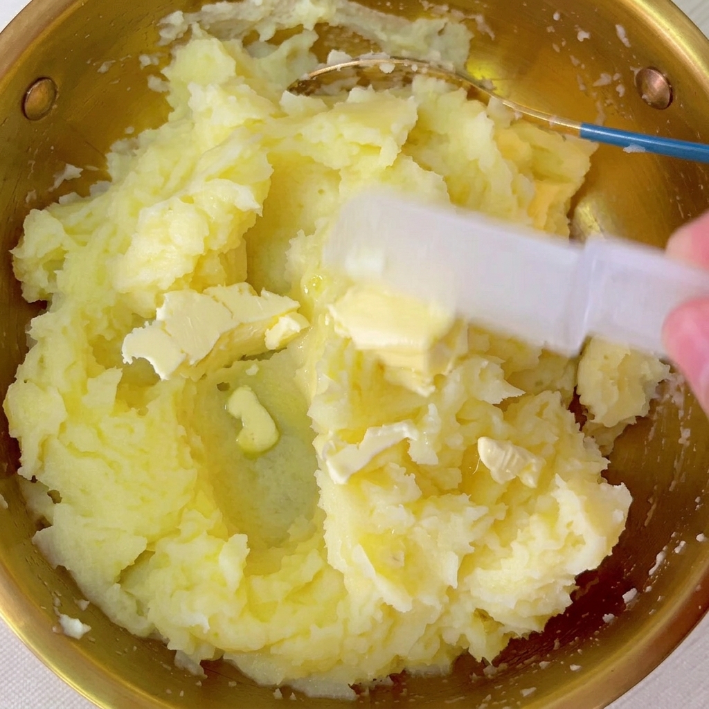 Morceaux de beurre en train dêtre mélangés dans le bol de purée de pommes de terre tiède.