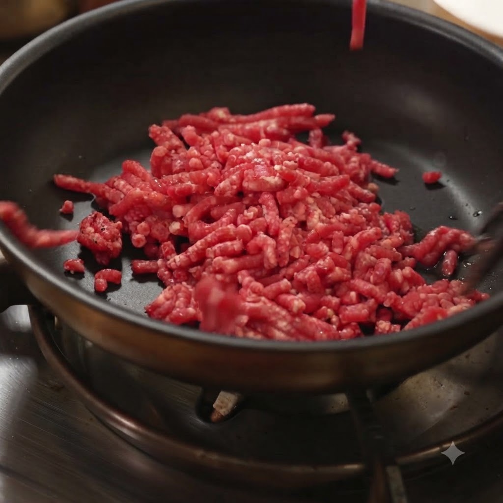 De la viande hachée crue ajoutée dans une poêle noire chaude sur une cuisinière.