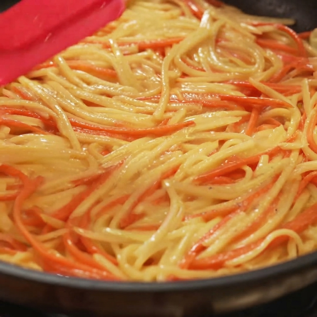 Une spatule étalant et aplatissant uniformément un mélange de pommes de terre et de carottes dans une poêle.