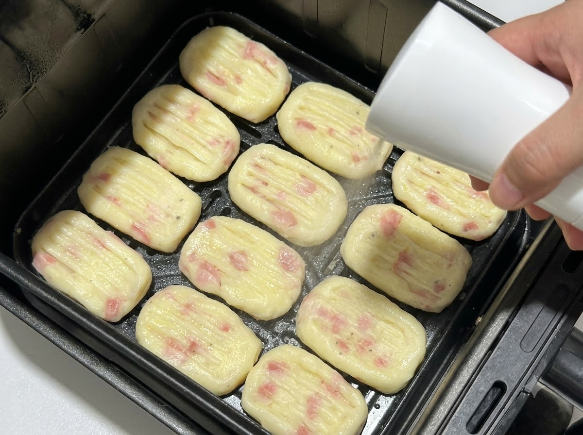 Galettes de pommes de terre façonnées disposées dans le panier dune friteuse à air tout en étant vaporisées dhuile à laide dun flacon pulvérisateur.