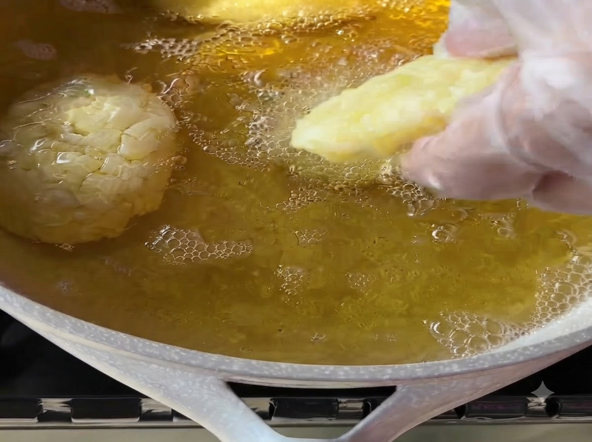 Une main gantée plaçant délicatement une galette de pommes de terre façonnée dans une poêle dhuile de cuisson chaude et bouillonnante.