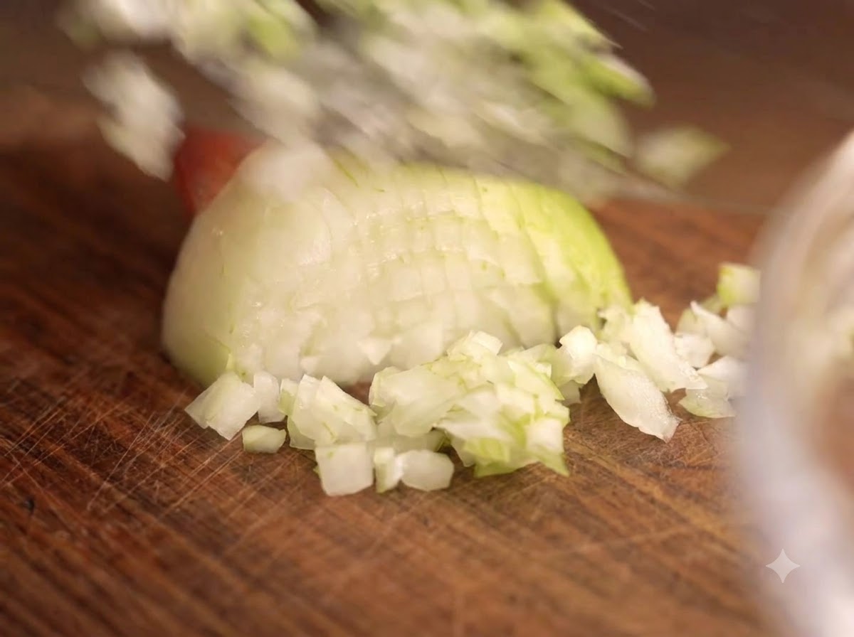 Un couteau coupant des oignons et de lail sur une planche en bois à côté dun bol en verre de viande.