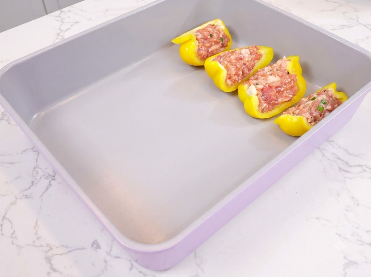 Moitiés de poivron jaune farcies de viande hachée assaisonnée et disposées proprement dans un plat de cuisson violet.