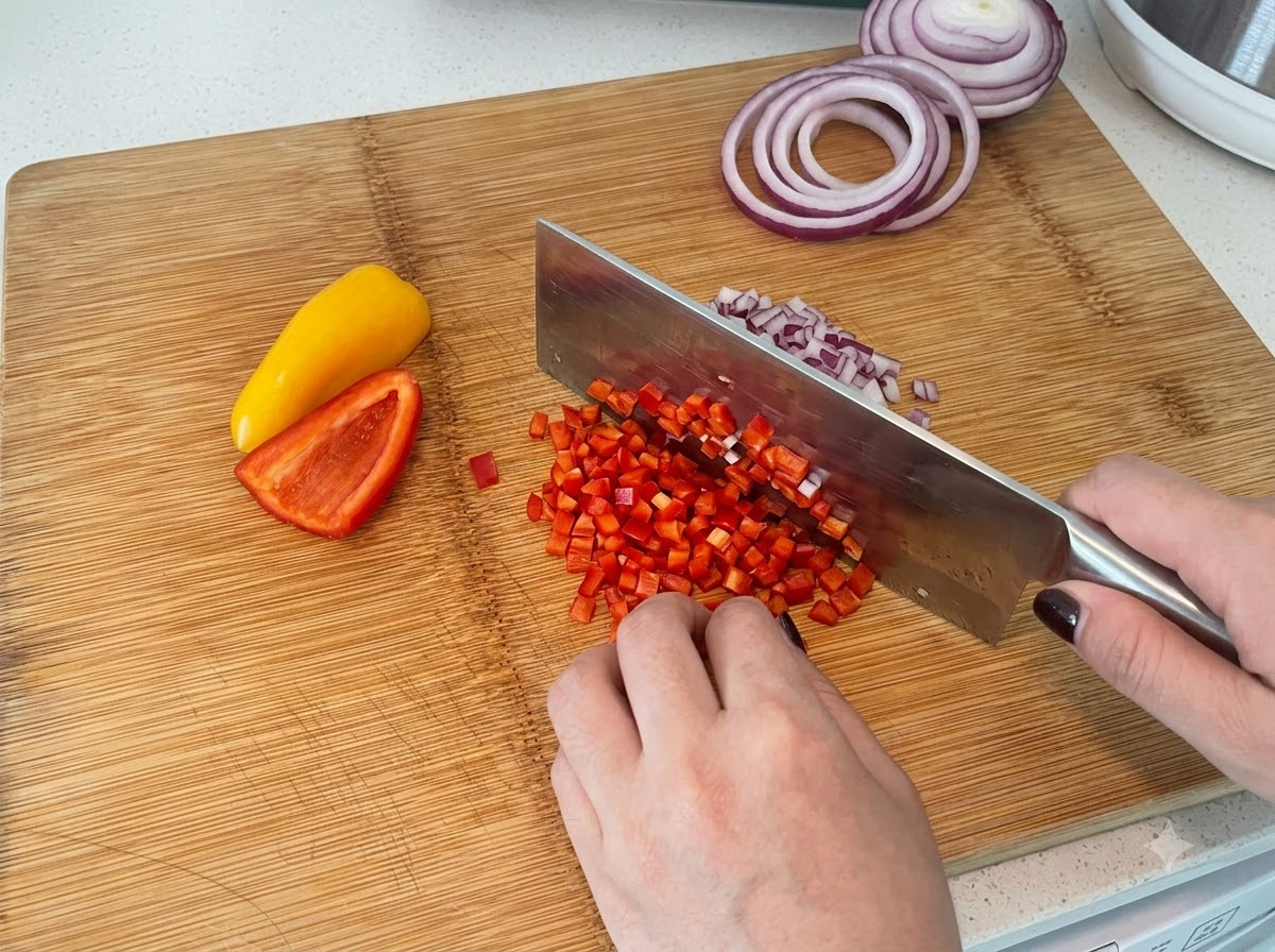 Poivrons rouges et jaunes coupés en dés sur une planche à découper en bois avec un couteau de cuisine.