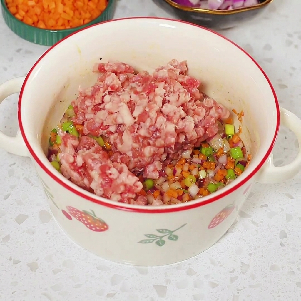 De la viande hachée crue placée sur le mélange de légumes assaisonné à lintérieur dun bol blanc.