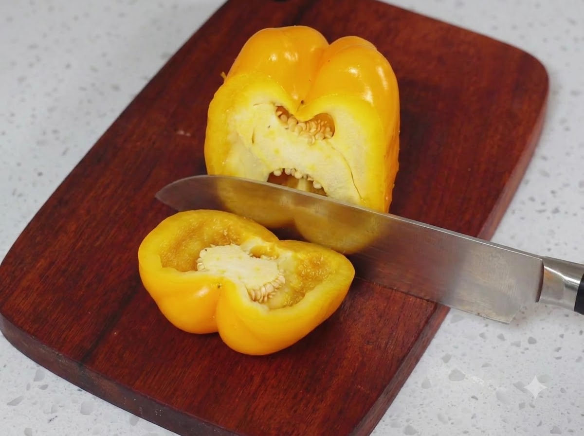 Un poivron jaune coupé en deux sur une planche à découper en bois avec un couteau de cuisine.