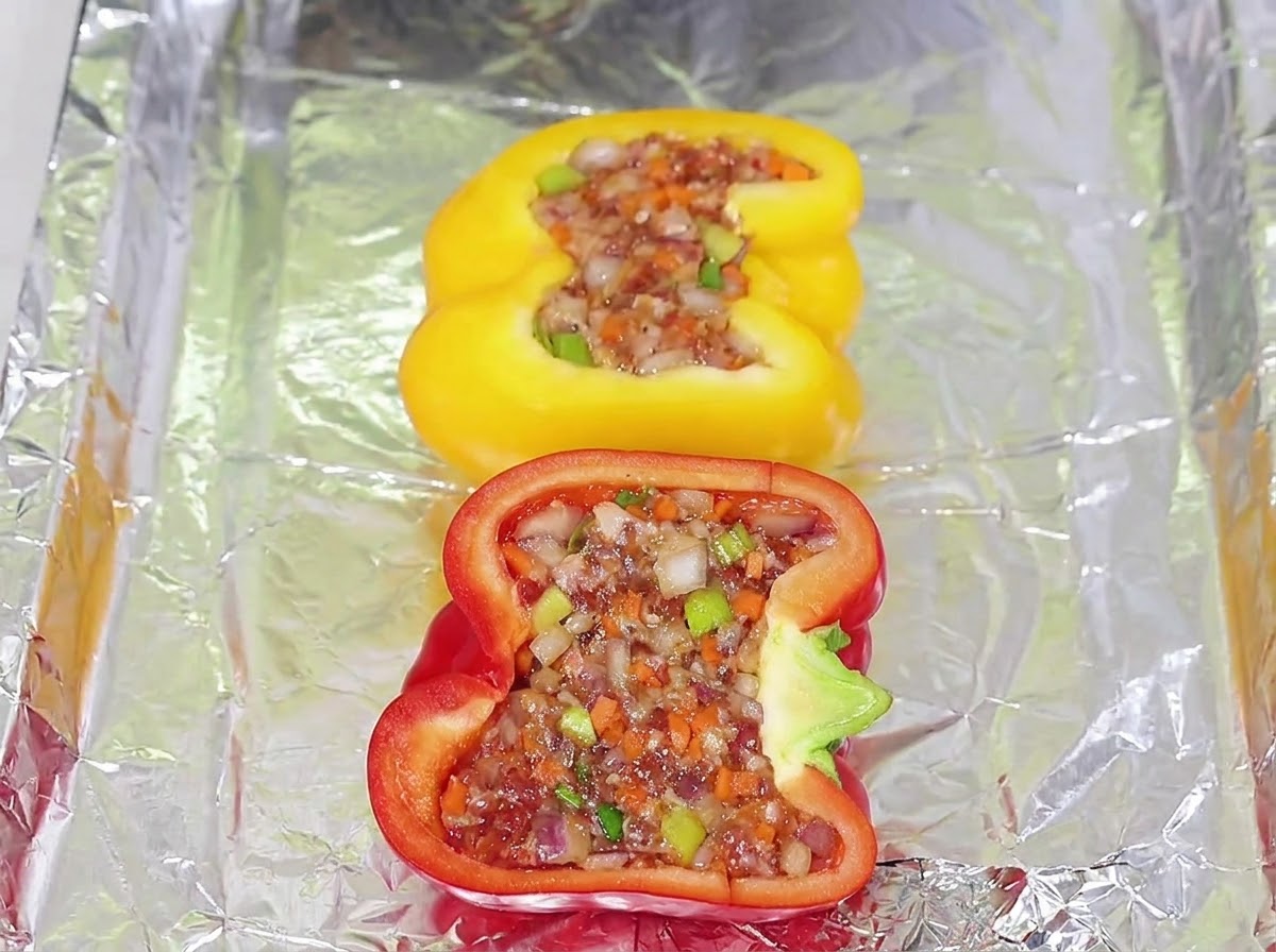 Des moitiés de poivrons jaunes et rouges farcies du mélange de viande disposées sur une plaque de cuisson recouverte de papier aluminium.