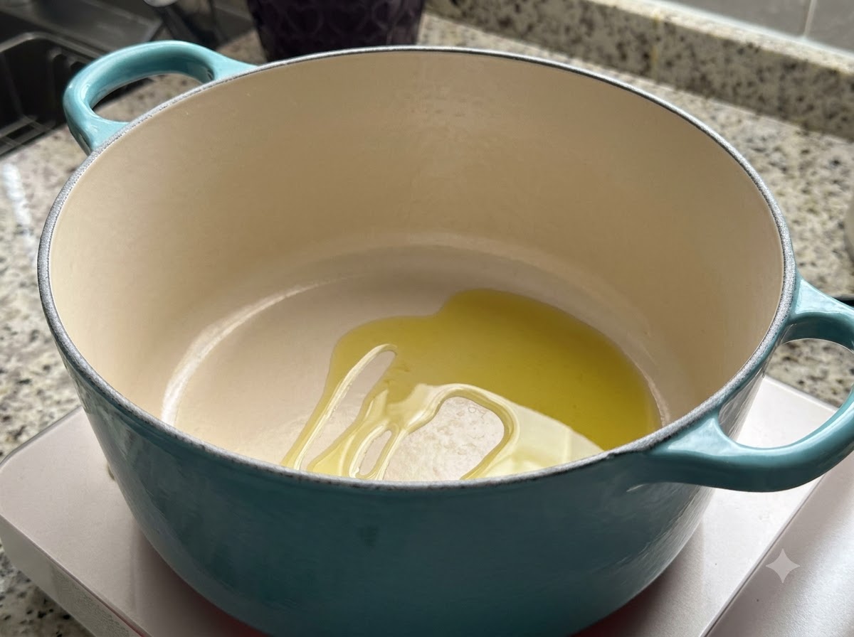 Une cocotte en fonte émaillée bleu sarcelle sur une table de cuisson avec un fond dhuile dolive en train de chauffer.