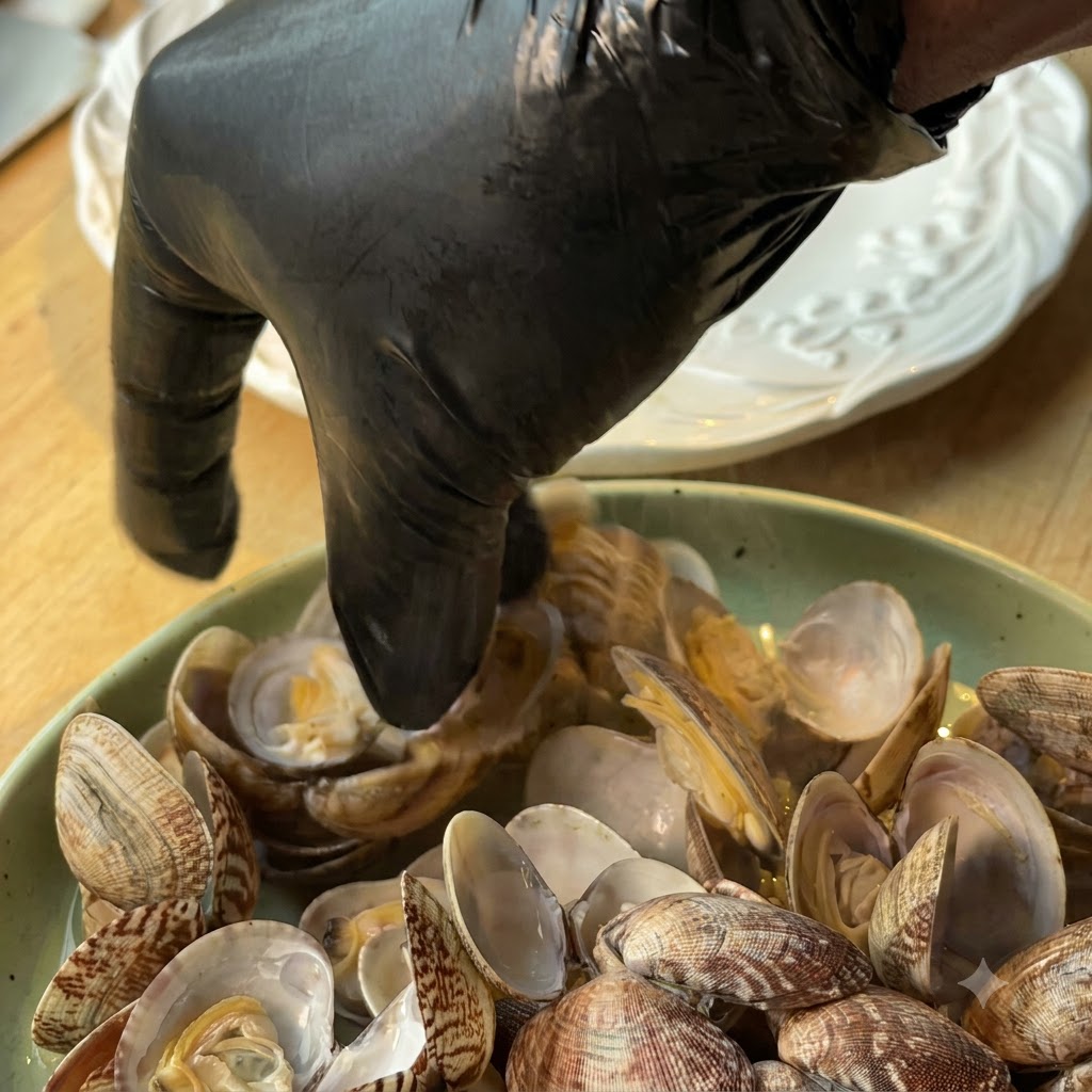 Une personne portant un gant noir récupérant la chair des palourdes de leurs coquilles dans une assiette.