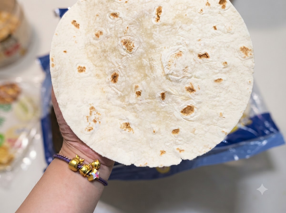 Gros plan sur une main tenant une tortilla de blé ronde présentant des taches brunes caractéristiques.