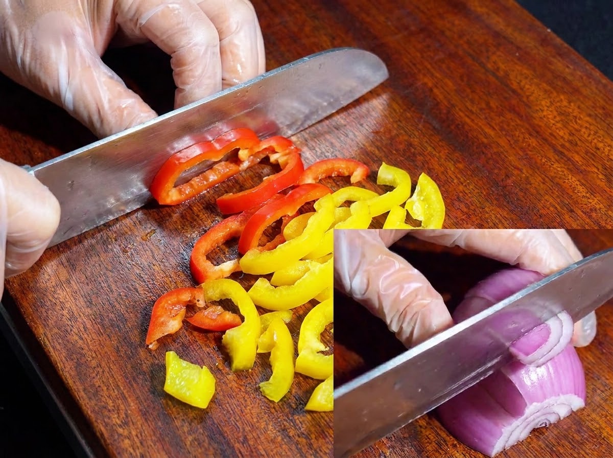 Un couteau coupant des poivrons colorés et un oignon rouge sur une planche à découper en bois.