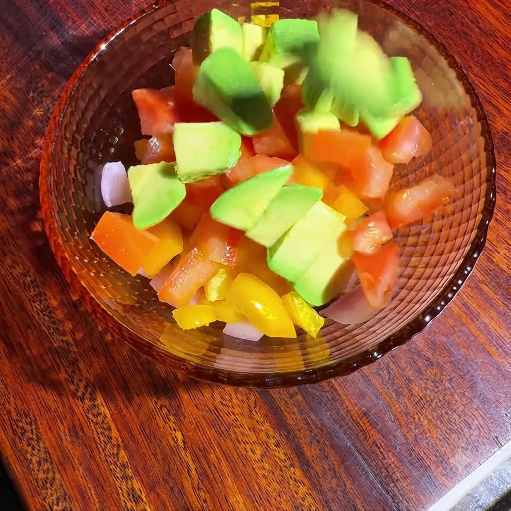 Un bol de légumes en dés et davocat en cours de mélange et dassaisonnement avec de lhuile et du jus de citron.