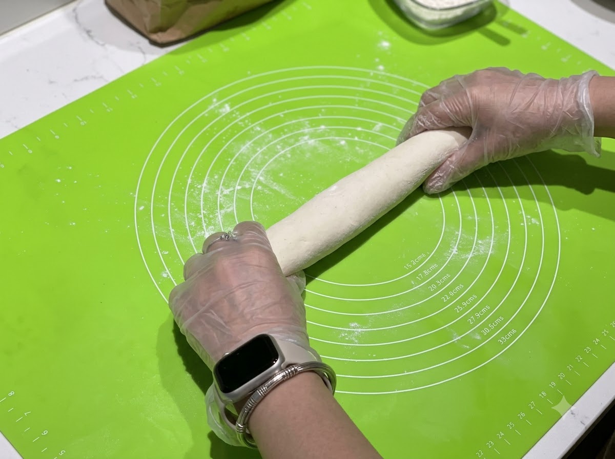 Des mains roulant un boudin de pâte sur un tapis en silicone vert avec des cercles de mesure.