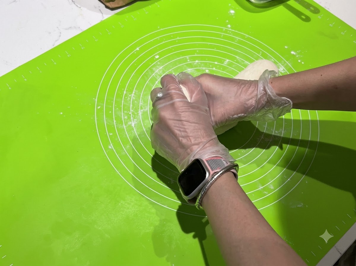 Des mains divisant une longue lanière de pâte en petits morceaux individuels sur un tapis vert.
