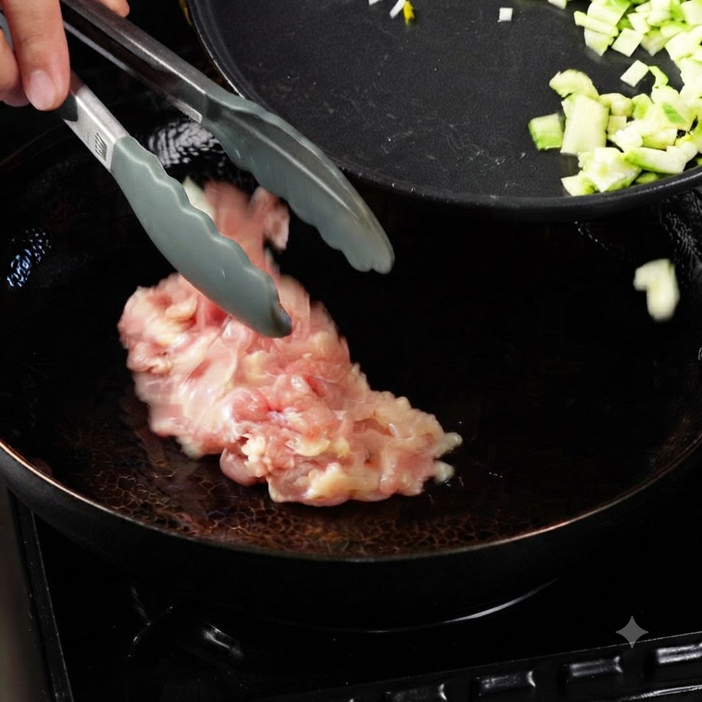 Des pinces plaçant des morceaux de poulet cru dans un wok chauffé avec de lhuile, à côté dune poêle contenant des légumes coupés en dés.