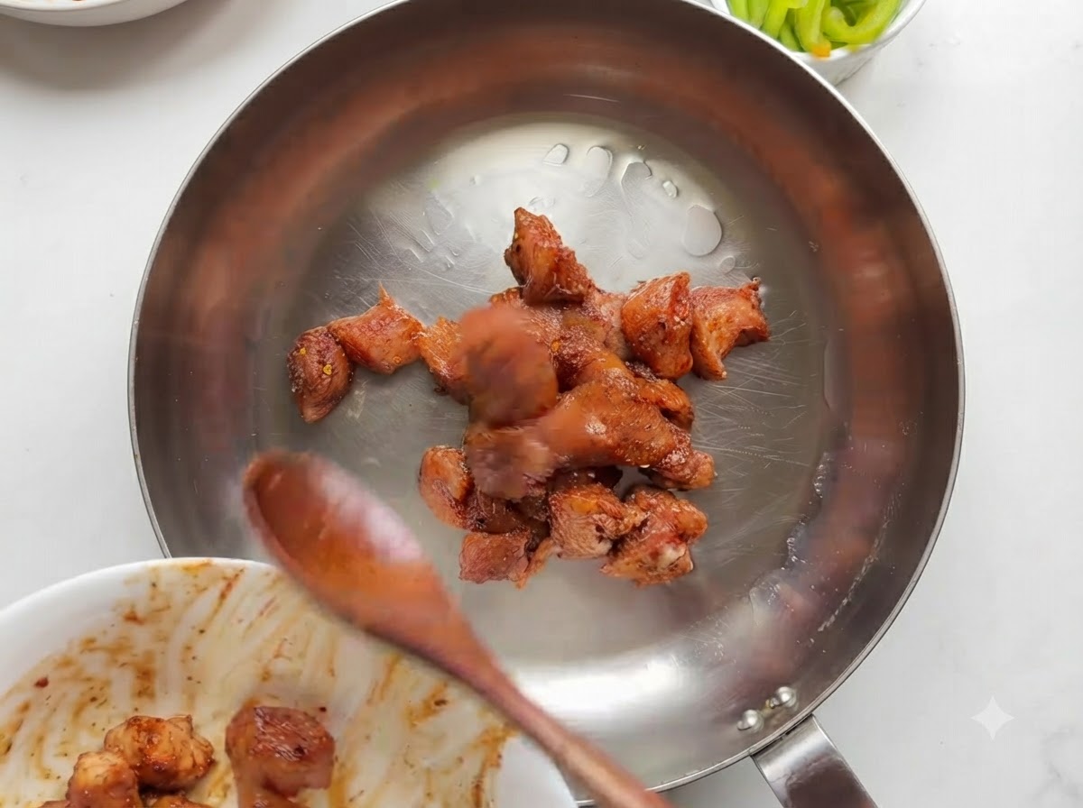 Des morceaux de poulet marinés qui cuisent et dorent dans une poêle en acier inoxydable.