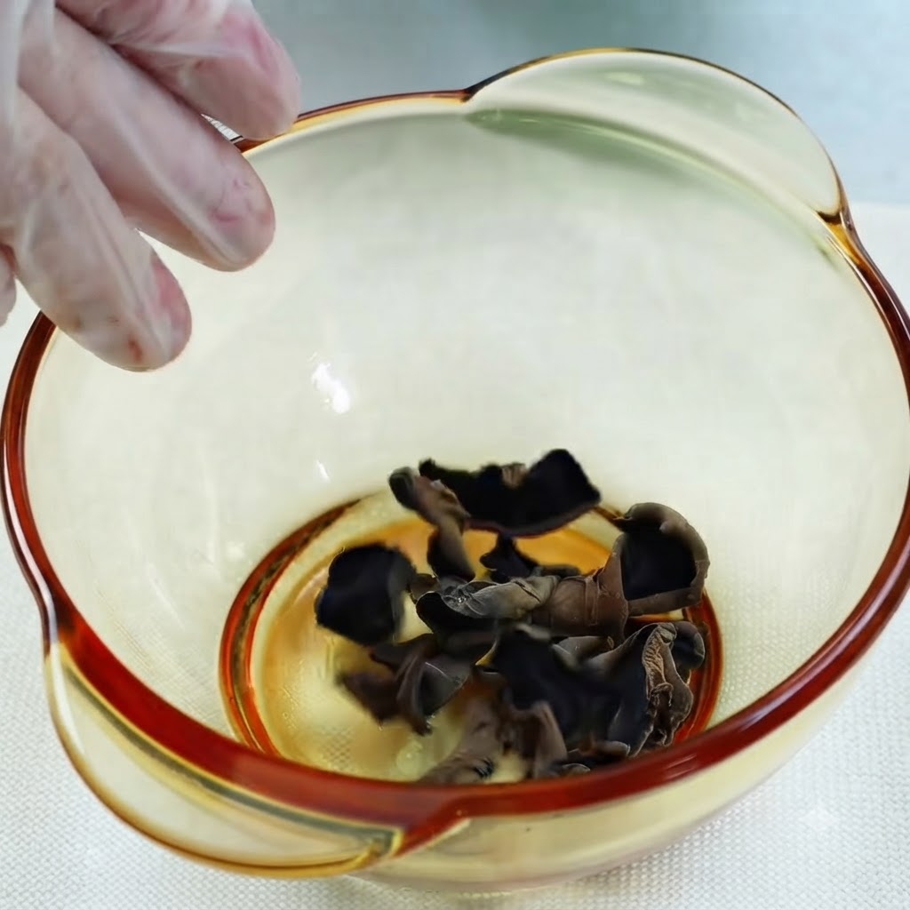 De leau versée dune tasse à mesurer en verre dans un bol de champignons noirs auricules séchés.
