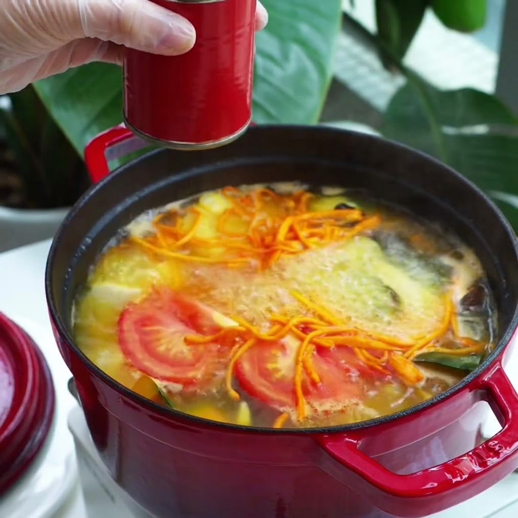 Une cuillerée dassaisonnement en pâte rouge ajoutée dans une marmite de soupe de légumes bouillante.