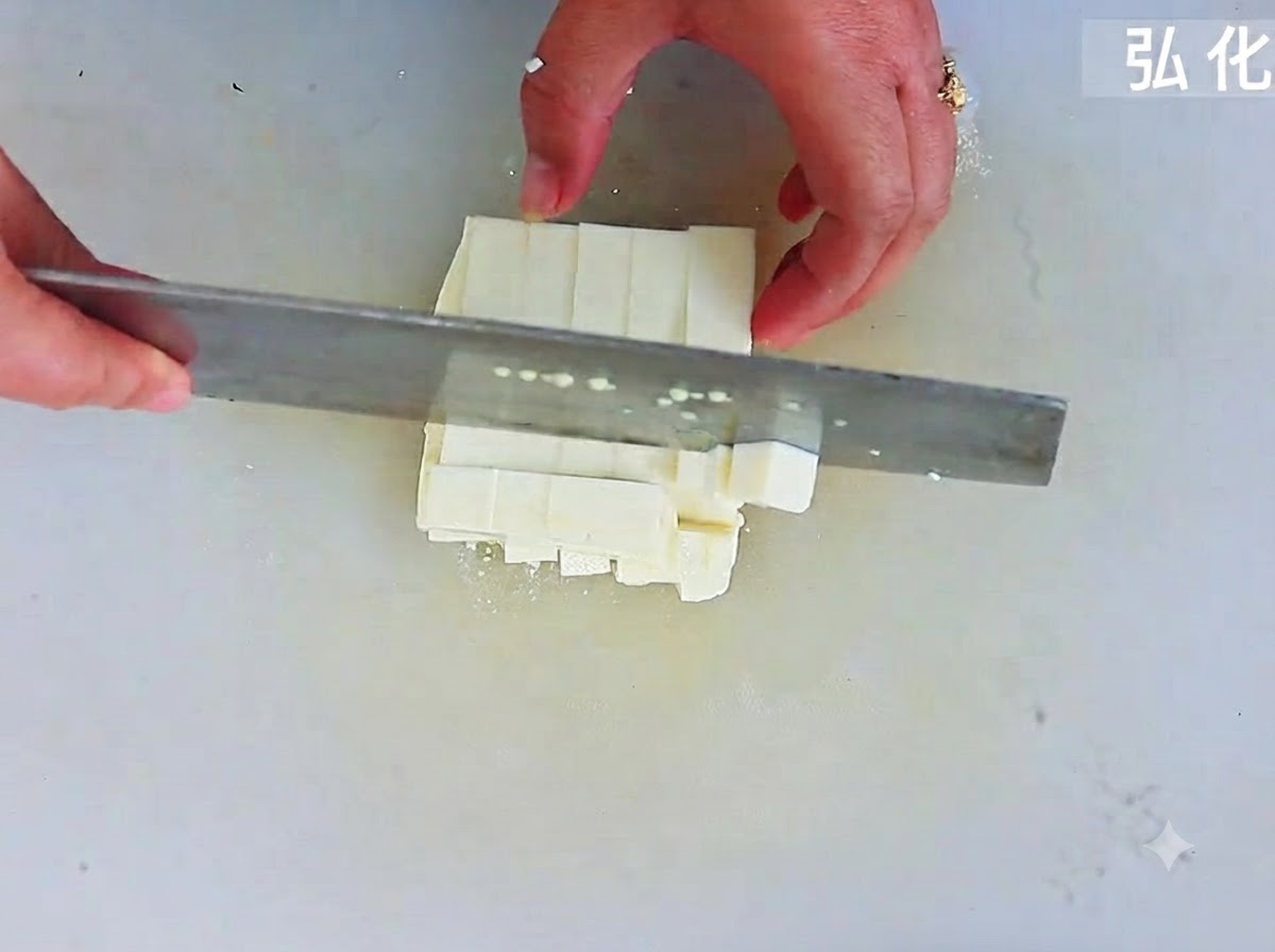 Du tofu soyeux découpé en cubes réguliers à laide dun grand couteau sur une planche à découper.