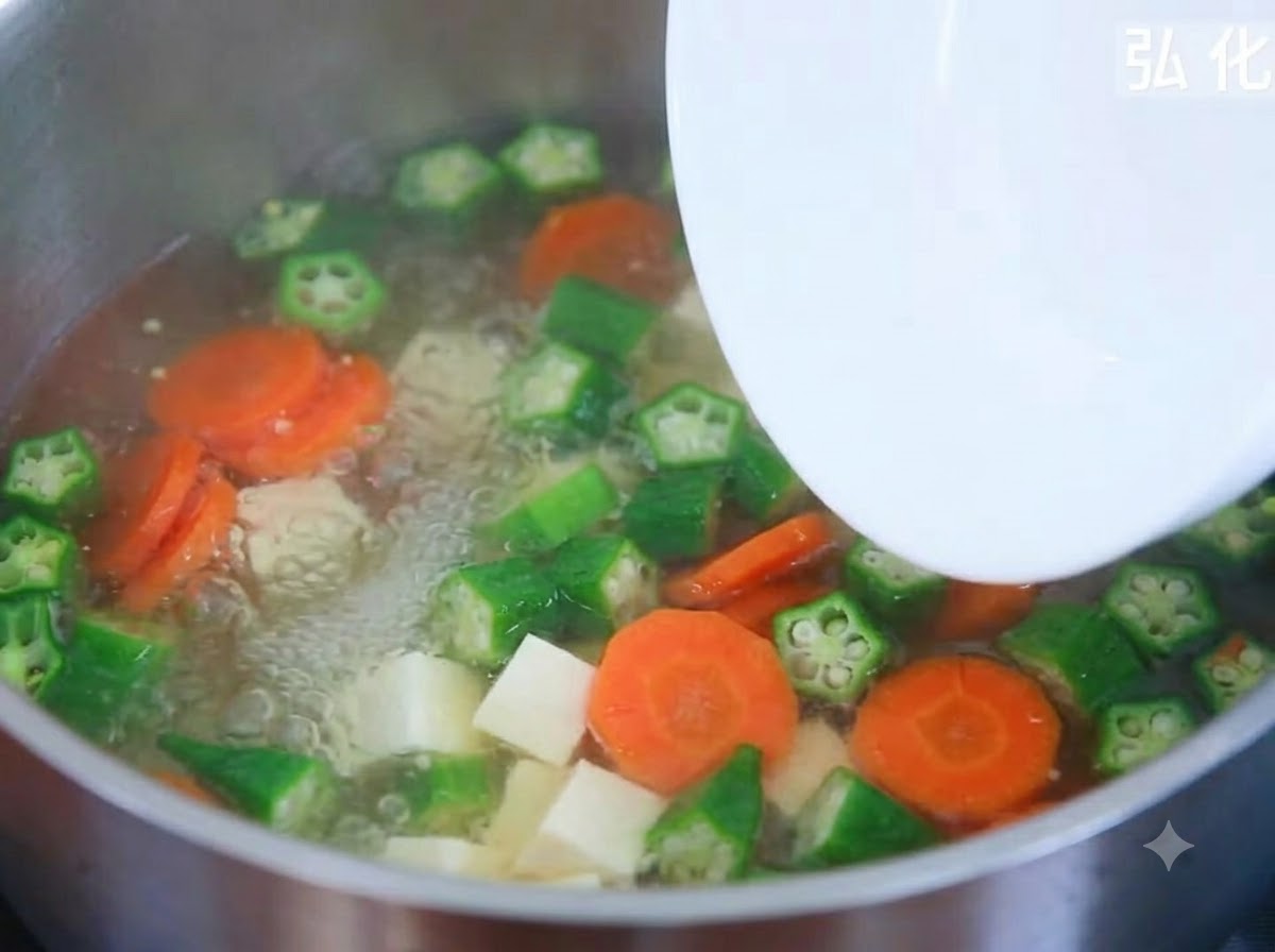 Des cubes de tofu soyeux ajoutés depuis une assiette dans une casserole de soupe de légumes frémissante.