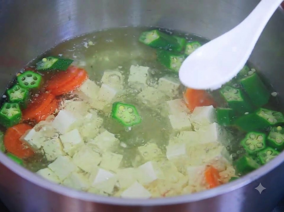 Une cuillère blanche contenant du sel au-dessus dune casserole de soupe de tofu, gombo et carotte.