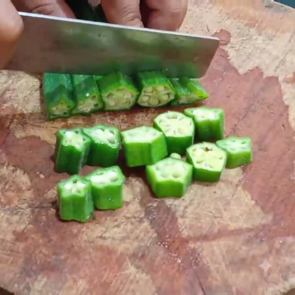 Un couteau de cuisine coupant des gombos blanchis en rondelles régulières sur une planche à découper en bois.