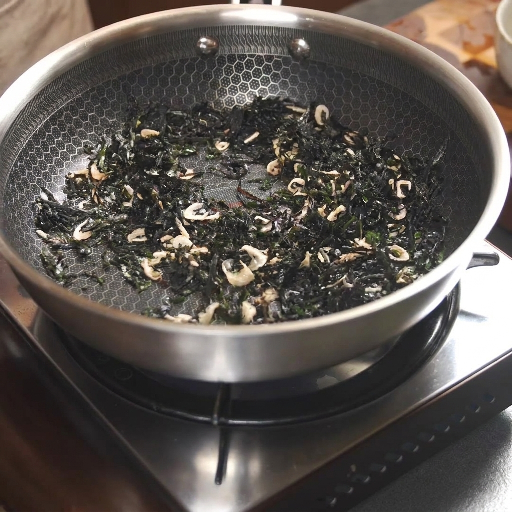 Algues séchées et petites crevettes séchées en train dêtre sautées à lintérieur dune poêle à laide de baguettes.