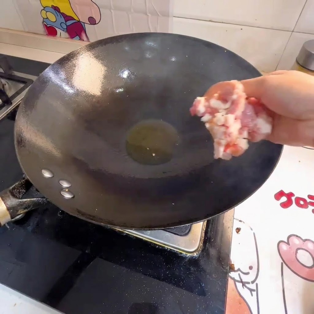 Une main dépose de la viande hachée dans un wok contenant de lhuile chaude.