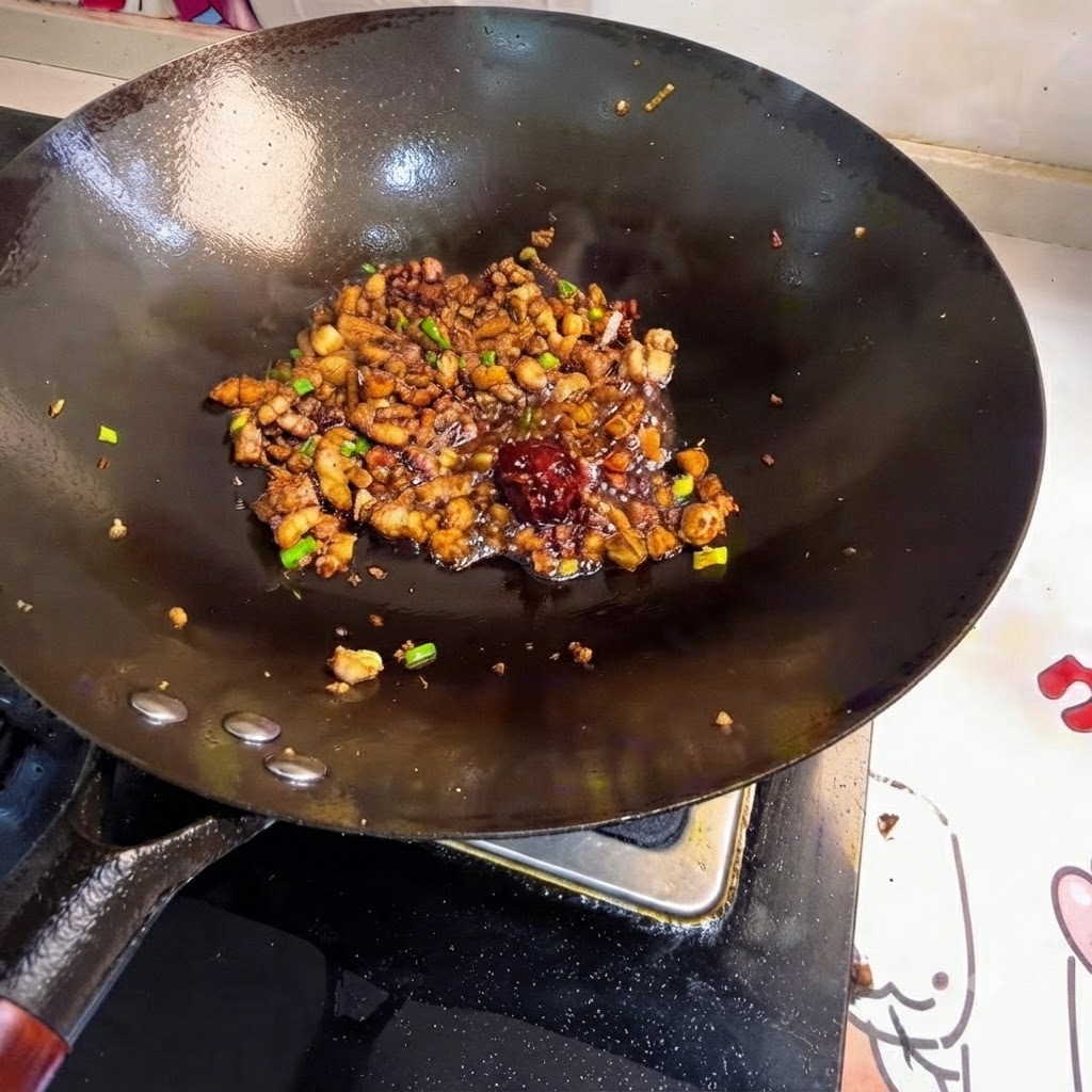 Une cuillerée de pâte de haricots placée au milieu de la viande sautée dans le wok.