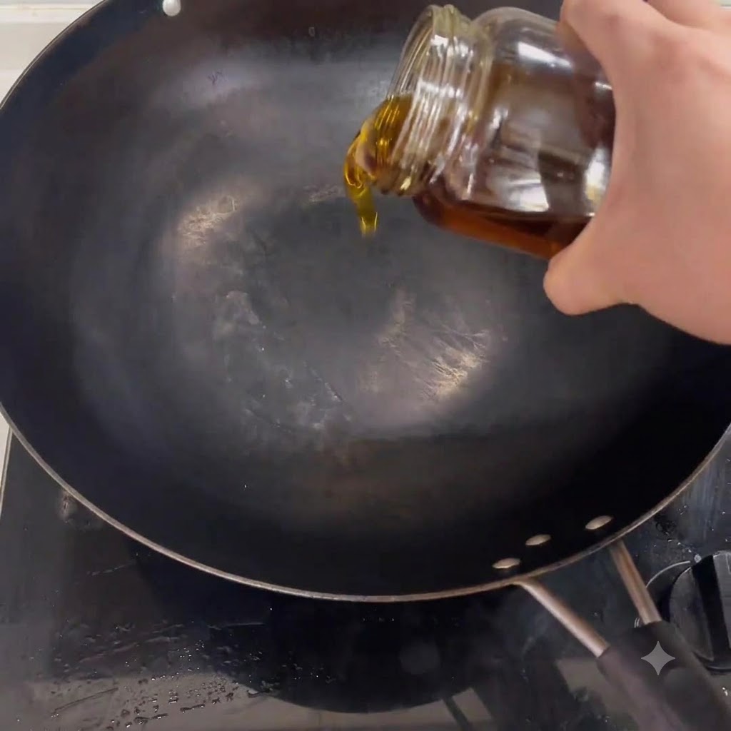 Huile de cuisson versée depuis un pot en verre dans un wok noir placé sur une cuisinière.