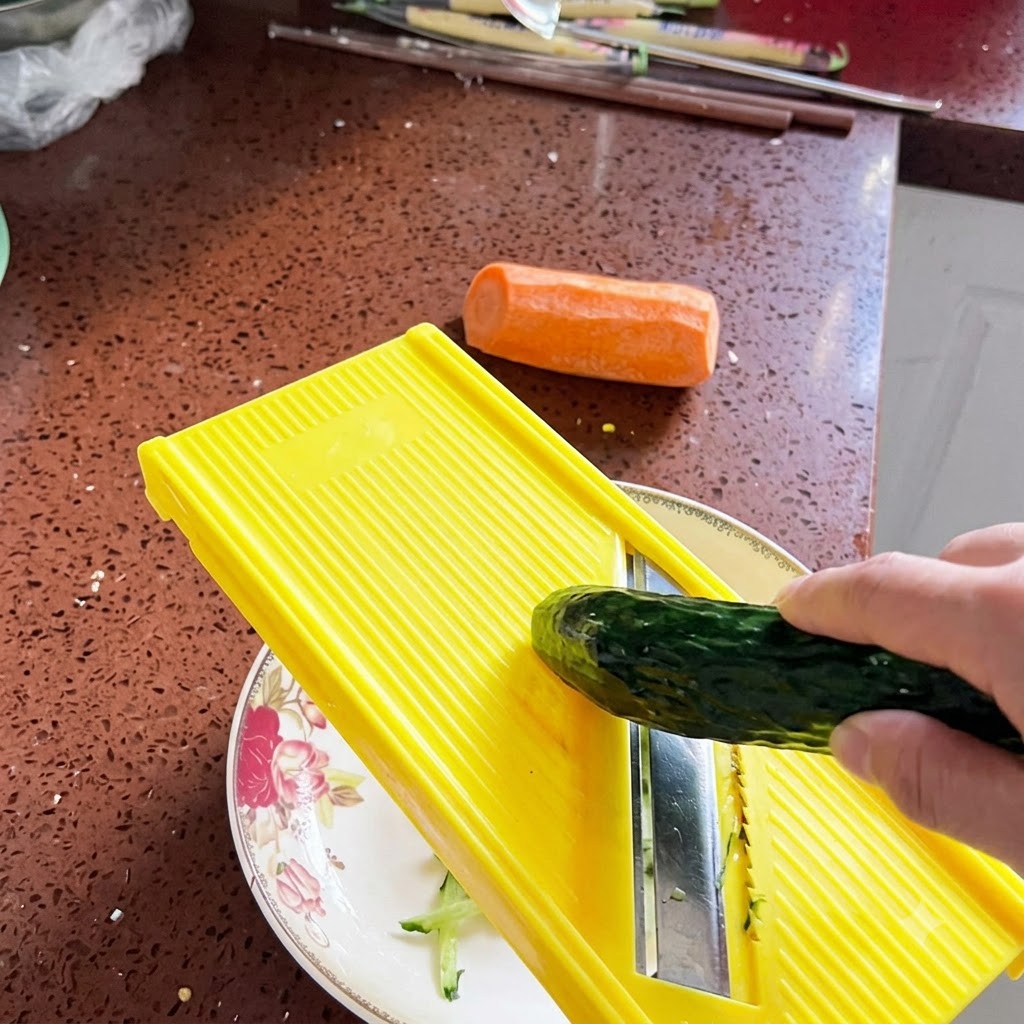 Un concombre frais râpé en fines lanières à laide dune mandoline jaune vif au-dessus dune assiette décorative.