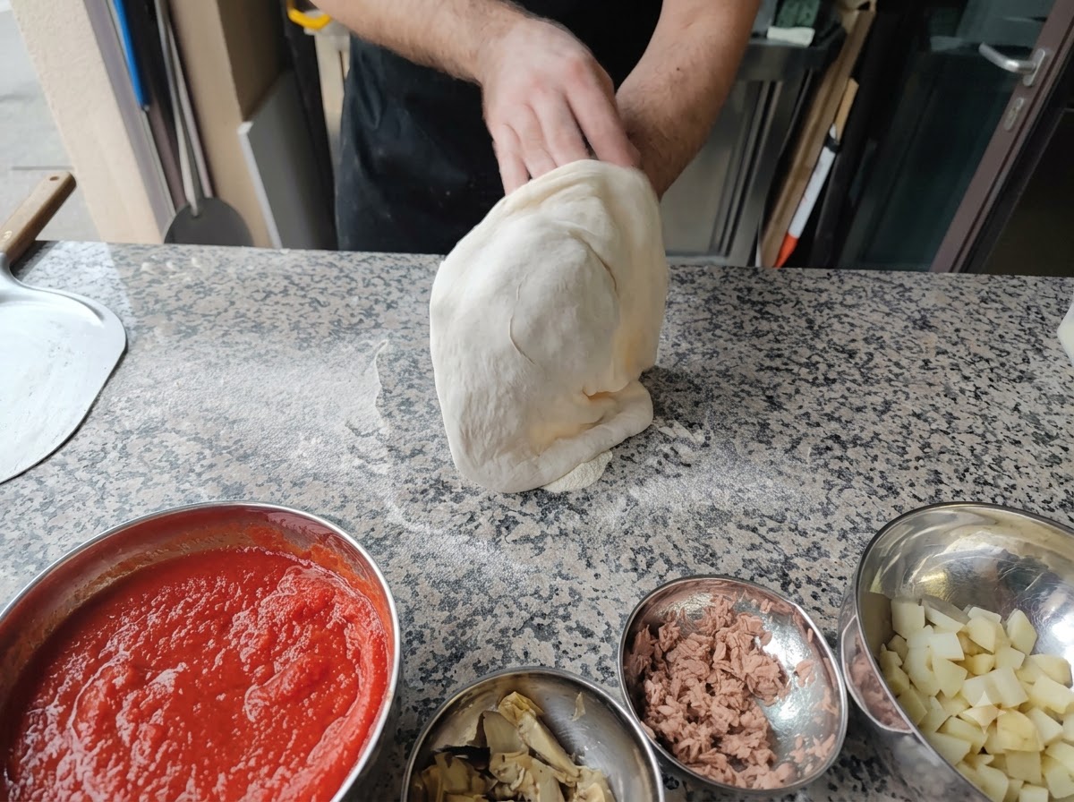Une personne étirant la pâte à pizza sur ses poings en lair.