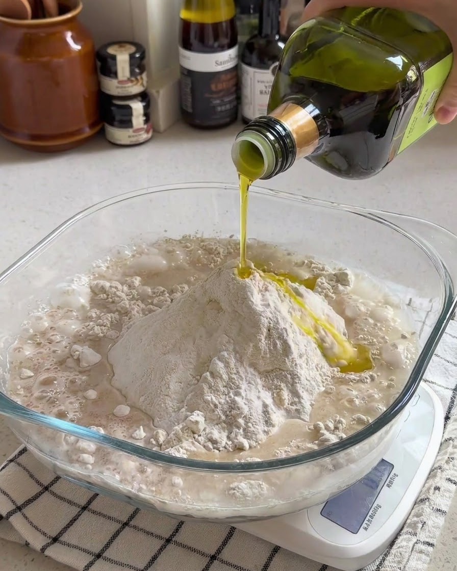 De lhuile dolive versée sur un mélange de farine et deau dans un bol en verre transparent sur une balance de cuisine.