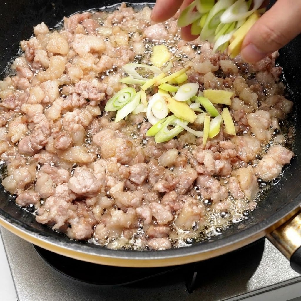 Cébette et gingembre hachés ajoutés directement dans la poêle avec le porc doré.
