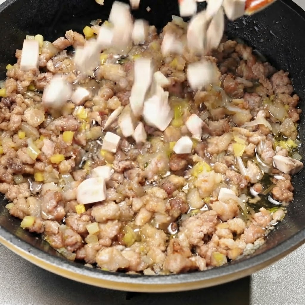 Dés de champignons ajoutés dans la poêle avec le mélange de viande assaisonné.